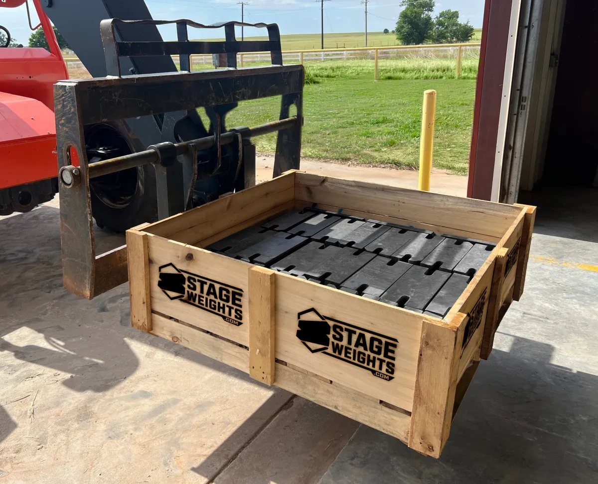 A forklift carrying a wooden Stage Weights crate filled with stacked steel counterweights